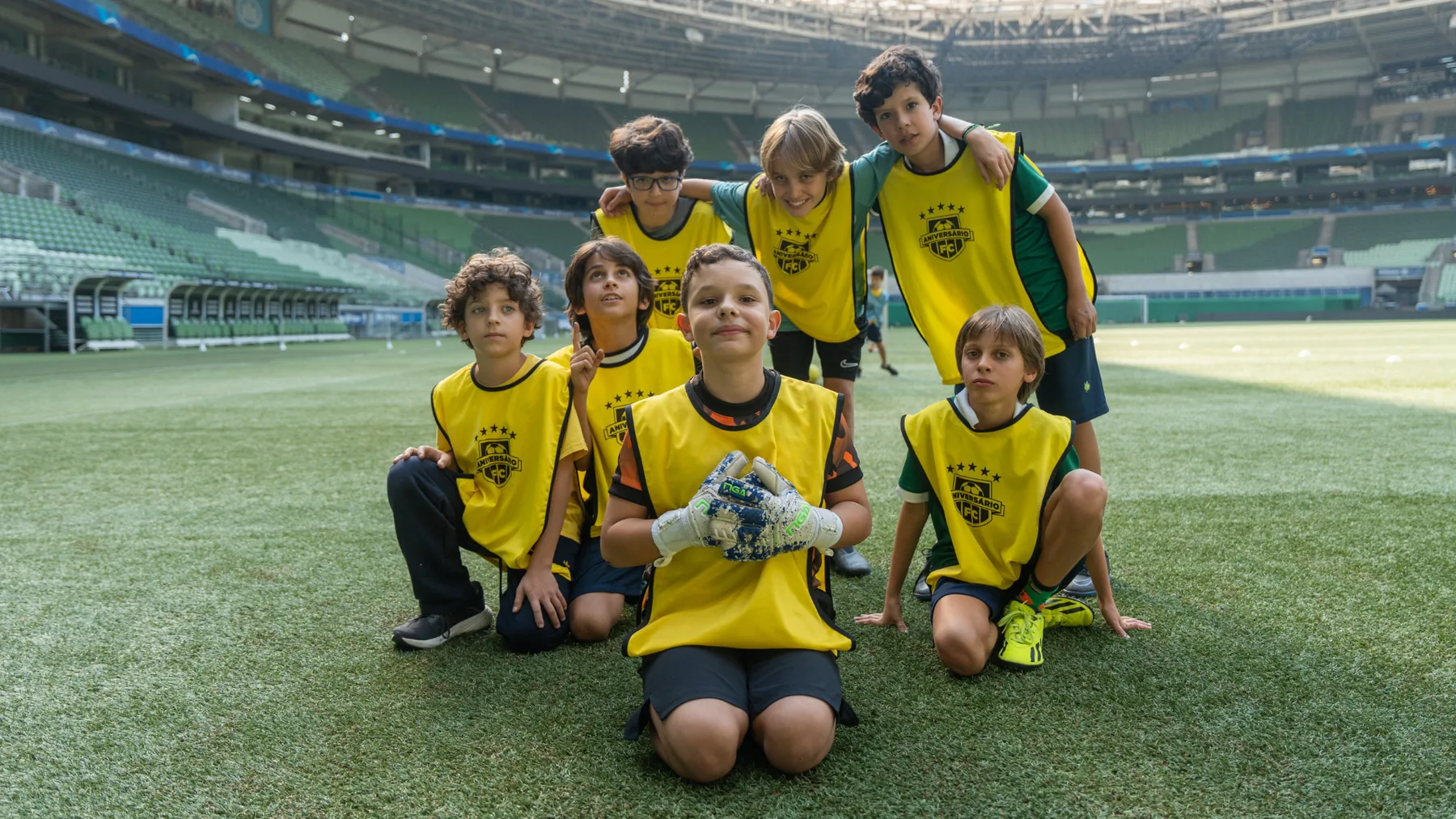 Time de crianças com coletes do Aniversário FC posando no gramado do estádio