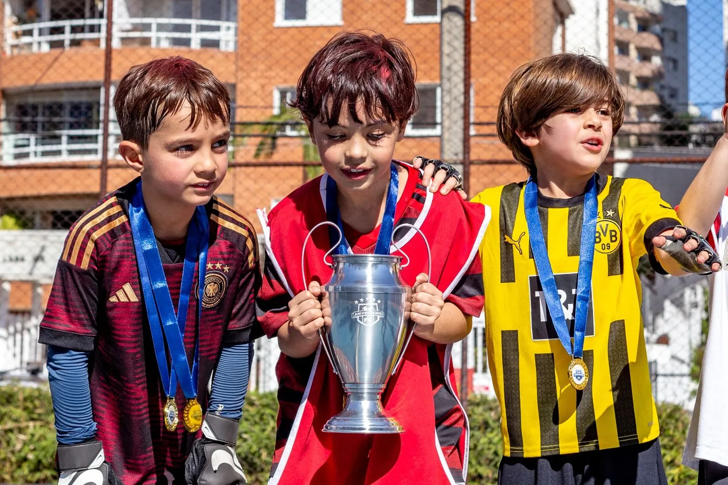Crianças com medalhas segurando a réplica da taça